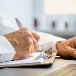 Close-up of a doctor writing notes on a clipboard in a well-lit office.
