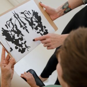 Hands holding a clipboard with an inkblot for psychological analysis.